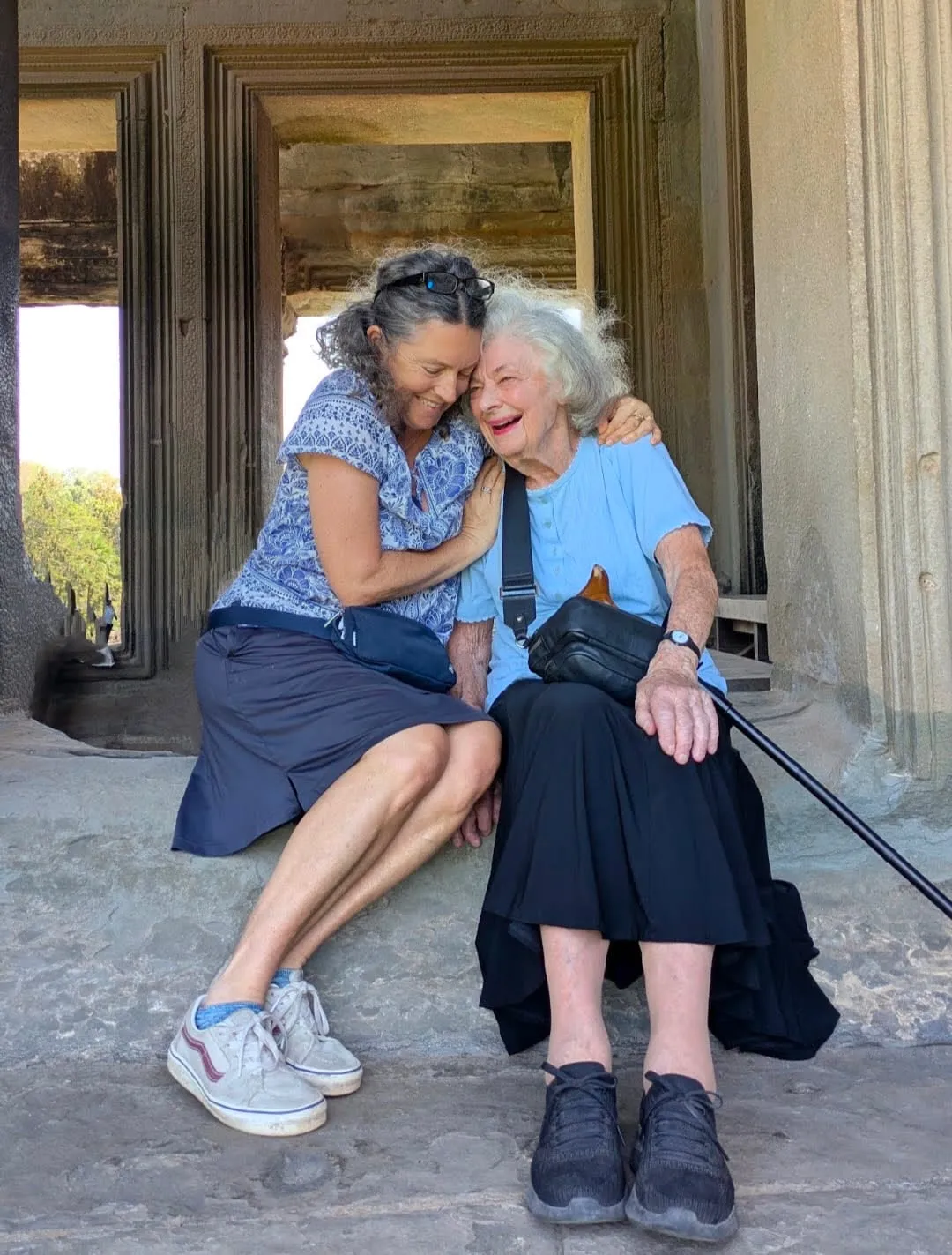 Kim and Dee laughing together, sitting on a stone step in a temple doorway