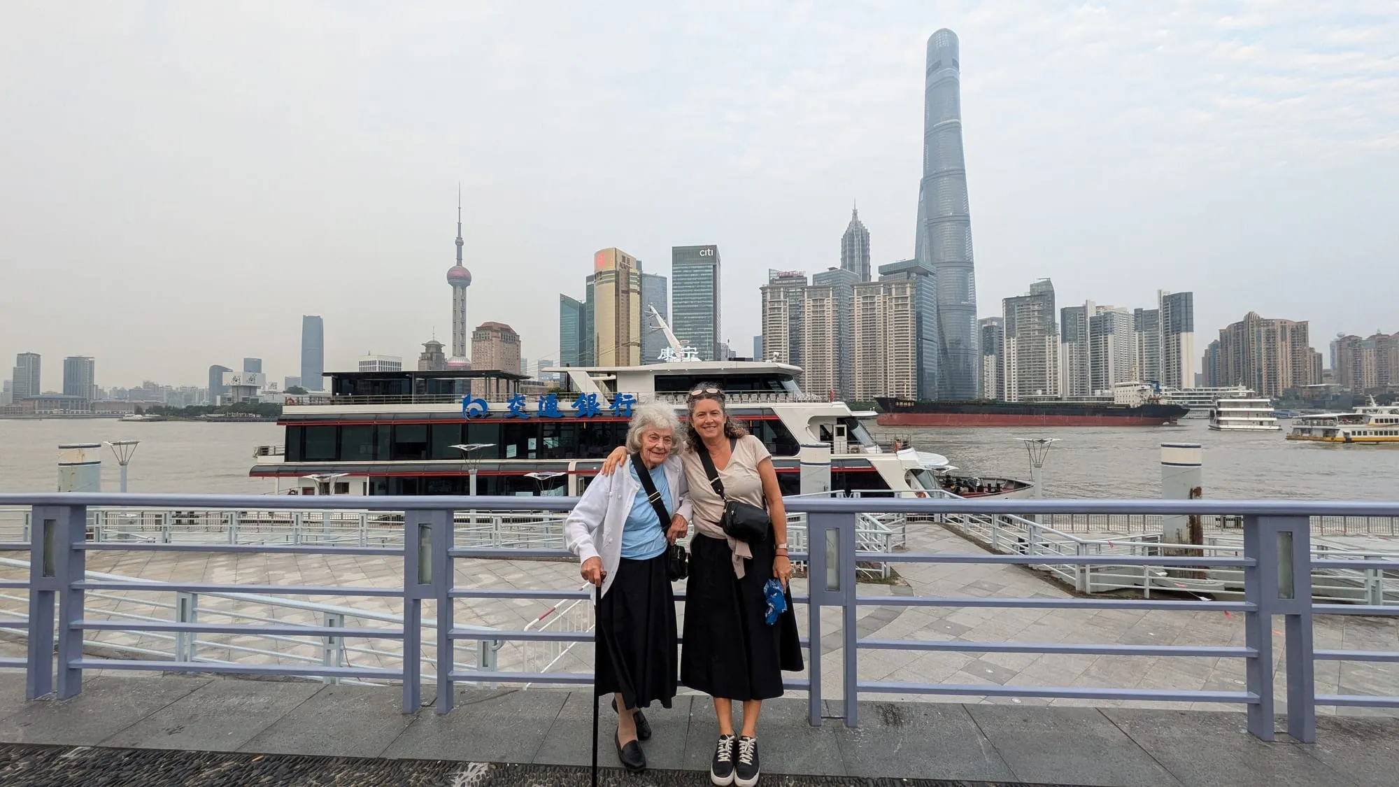 Dee and Kim at a riverside railing with the Shanghai skyline behind them